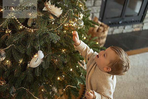 Der kleine Junge greift fröhlich nach oben  um den Weihnachtsbaum der Familie zu schmücken