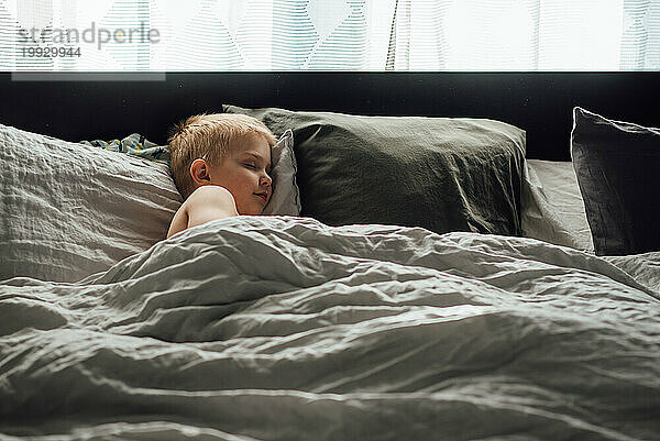 Weite Sicht auf einen kleinen Jungen  der friedlich auf einem großen Bett mit n ein Nickerchen macht