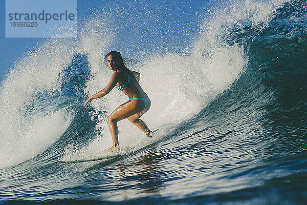 Ein Mädchen im Bikini surft auf einer Welle