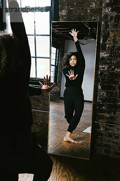Gemischte Rassen-Tänzerin posiert mit gestreckten Händen im Spiegel