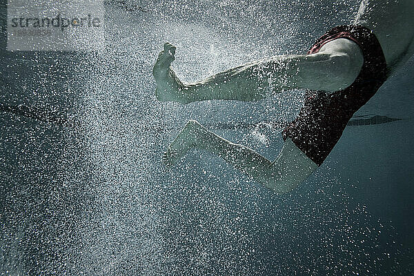 Ein Mann strampelt mit den Füßen  während er durch einen Pool schwimmt.