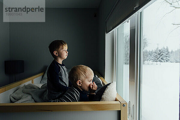 Helle Seitenansicht von kleinen Brüdern  die auf dem Bett sitzen und nach draußen schauen