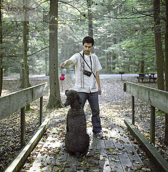 Ein junger Mann spielt mit seinem Standardpudelhund im Fowlers Hollow State Park in der Nähe von Newville  Pennsylvania