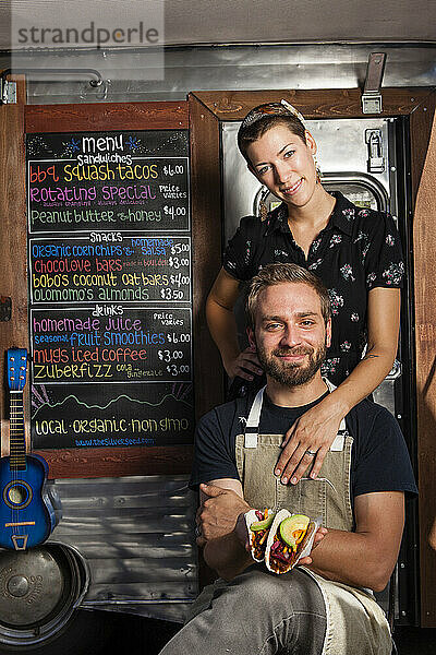 Der Silver Seed-Food-Trailer  der ausschließlich veganes Essen serviert. Die Besitzer und das Ehepaar Taylor Smith (Typ) und Melanie Boyna (Dame) halten einen Shredded Squash Taco in der Hand.