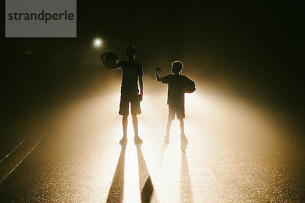 Brüder im Gegenlicht bei Nacht mit Basketbällen auf der Straße