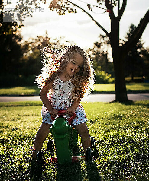 Glückliches kleines Mädchen mit langen Locken  das auf Spielzeug im Freien spielt