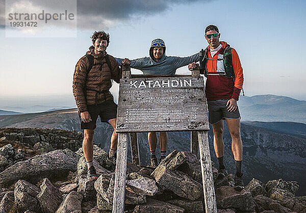 Drei männliche Freunde stehen am Gipfelschild des Katahdin  Appalachian Trail
