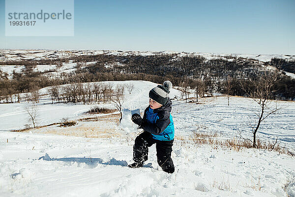Weite Sicht auf einen kleinen Jungen  der im Schnee einen steilen Hügel hinaufsteigt