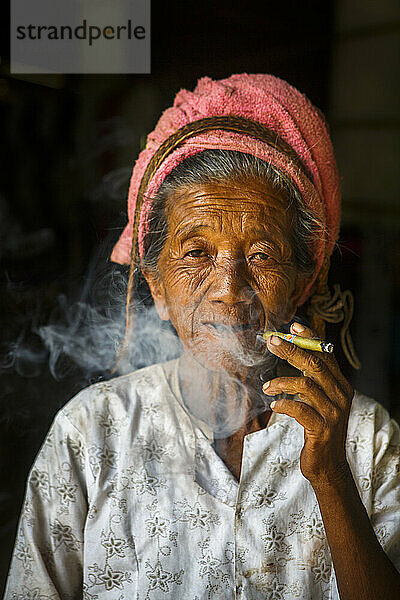 Porträt einer älteren Frau  die beim Rauchen einer Cheroot-Zigarre in die Kamera blickt  Shan State  Myanmar