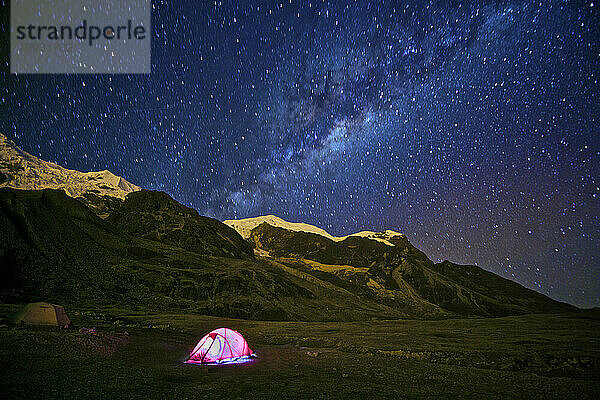 A tent lit at night and the Milky Way Galaxy at Illimani base camp near La Paz  Bolivia