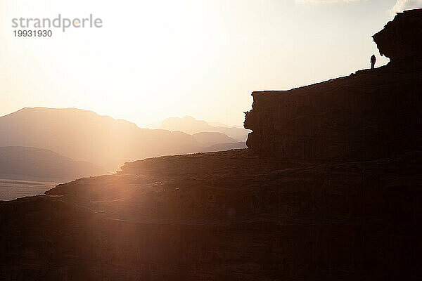 Silhouette eines Mannes  der bei goldenem Sonnenuntergang auf dem Gipfel des Berges spaziert