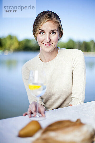 Eine Frau genießt ihr Abendessen an einem Tisch im Freien mit einem malerischen See im Hintergrund.