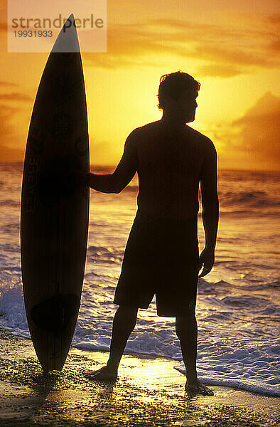 Surfer mit Surfbrett  Silhouette gegen die untergehende Sonne an der Nordküste von Oahu  HI  USA.