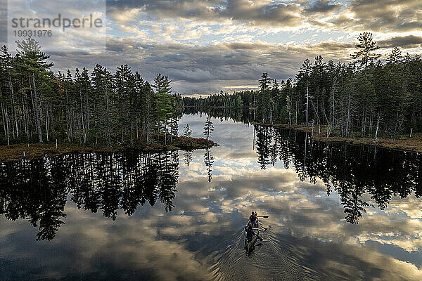 Zwei Personen paddeln in einem Kanu über einen ruhigen Teich in Maine