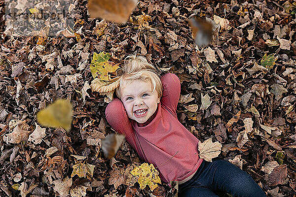 Lächelndes Kind  das im Laubhaufen liegt  während Herbstblätter fallen
