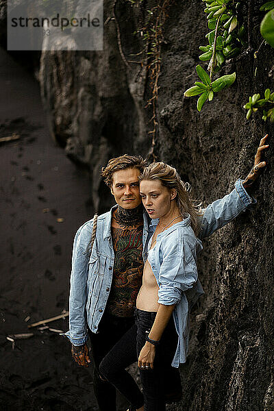 Junges schönes Paar am schwarzen Sandstrand  Bali. Tätowierter Mann.