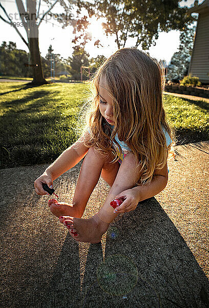 Entzückendes Kleinkind mit langen Locken  das draußen Zehennägel malt