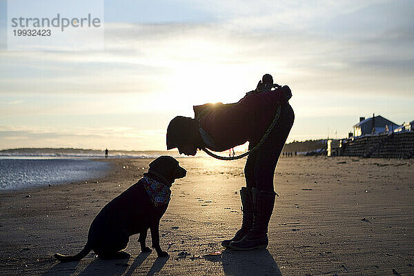 Eine Frau beugt sich vor  um ihren Hund am Higgins Beach  Scarborough  Maine zu küssen. (Silhouette)