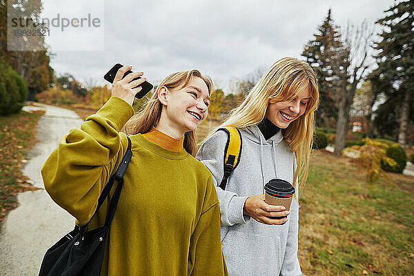 Zwei glückliche junge Mädchen mit einem Getränk zum Mitnehmen  die telefonieren