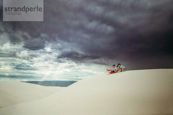 Zwei Kinder rodeln auf weißem Sand mit Gewitterwolken darüber