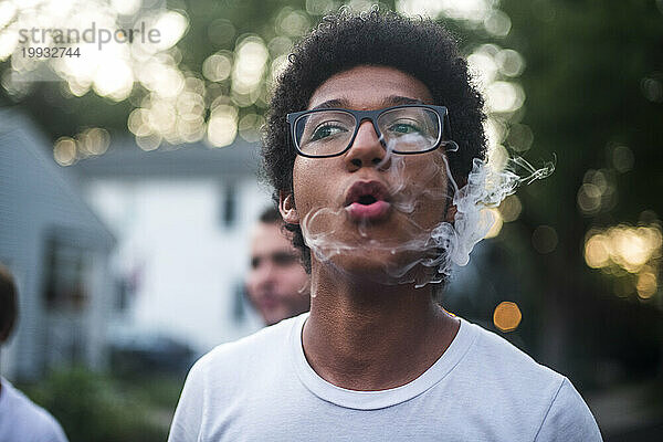Junger Mann atmet eine Rauchwolke aus