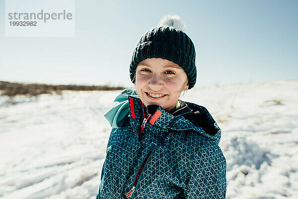 Teenager-Mädchen mit Winterausrüstung und Hut lächelt mit einem einfachen Lächeln in die Kamera