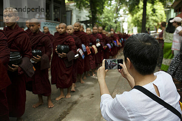 Tourist fotografiert eine große Gruppe von Mönchen beim Spaziergang im Mahagandhayon-Kloster  Amarapura  Myanmar