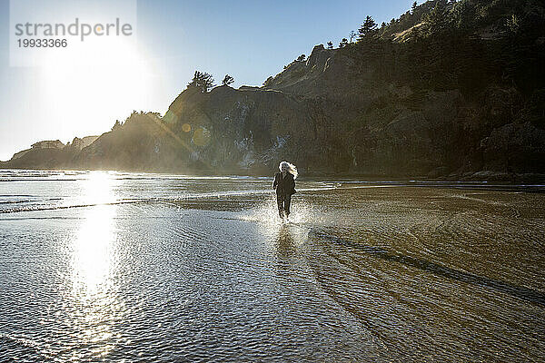 USA  Oregon  Newport  Frau läuft am Sandstrand und spritzt Wasser