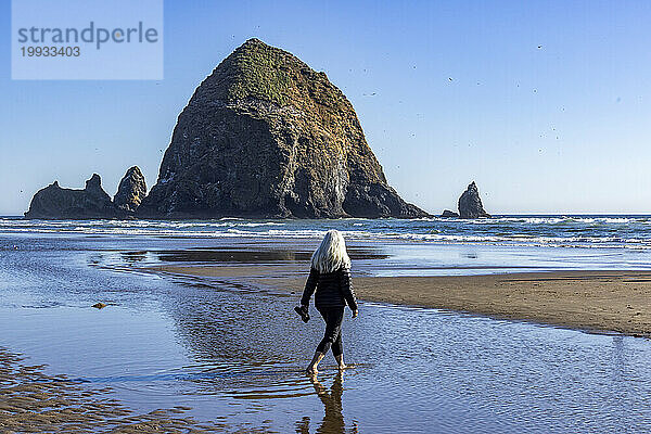 USA  Oregon  Rückansicht einer Frau  die in der Nähe des Haystack Rock am Cannon Beach spaziert