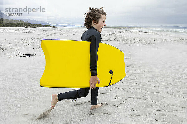 Junge (10-11) läuft mit Bodyboard am Strand