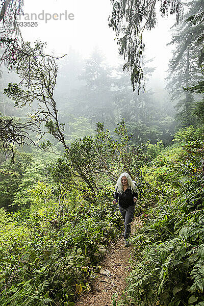 Ältere Frau wandert mit Nordic-Walking-Stöcken auf einem Hügel