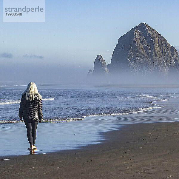 USA  Oregon  Rückansicht einer Frau  die im Morgennebel in der Nähe des Haystack Rock am Cannon Beach spaziert