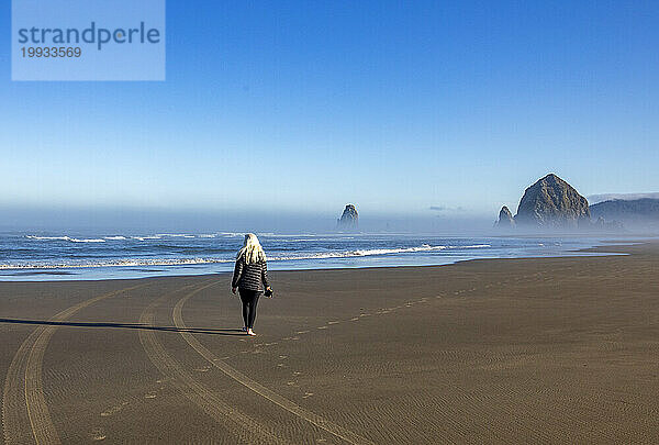 USA  Oregon  Rückansicht einer Frau  die im Morgennebel in der Nähe des Haystack Rock am Cannon Beach spaziert