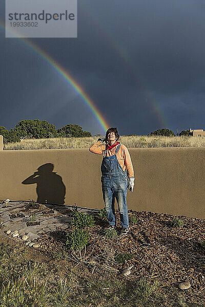 USA  New Mexico  Santa Fe  Porträt einer Frau im Garten mit doppeltem Regenbogen im Hintergrund