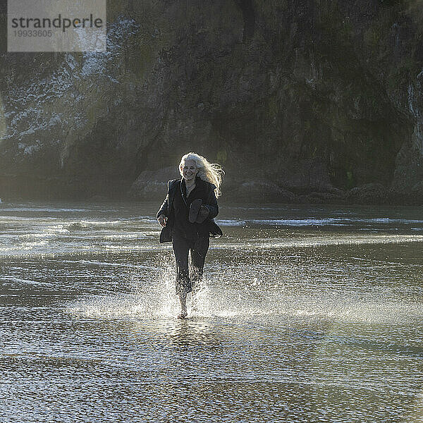 USA  Oregon  Newport  Frau läuft am Sandstrand und spritzt Wasser