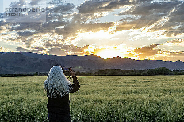Ältere Frau fotografiert den Sonnenaufgang über den Bergen