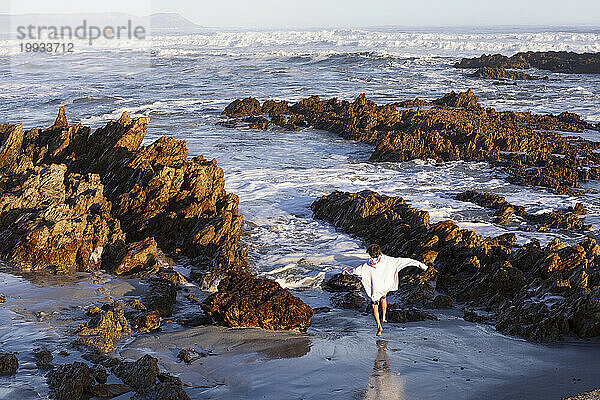 Südafrika  Hermanus  Junge (10-11) läuft zwischen Felsen am Strand von Kammabaai