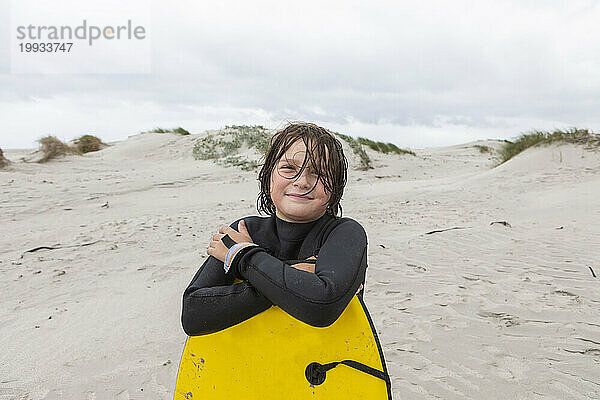 Lächelnder Junge (10-11) hält Bodyboard am Strand