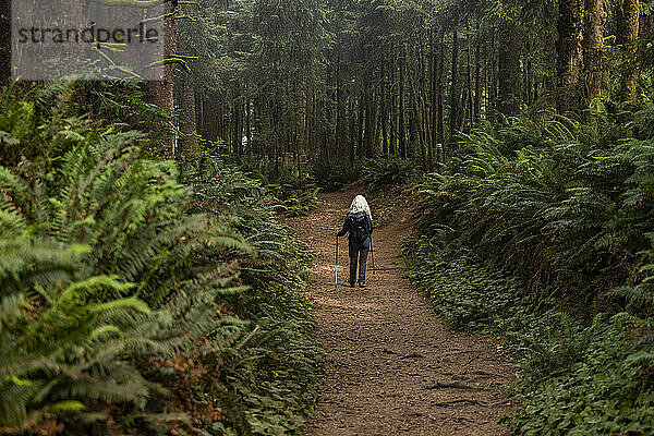 Ältere Frau wandert mit Nordic-Walking-Stöcken im Wald