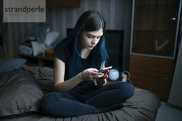 Ernsthafte Frau benutzt Smartphone  während sie im Bett sitzt