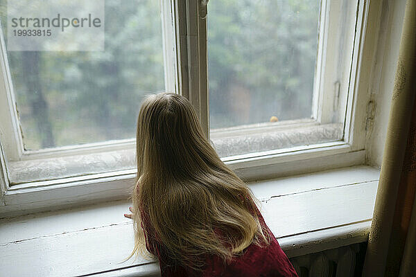 Mädchen (4-5) schaut neugierig durch das Fenster