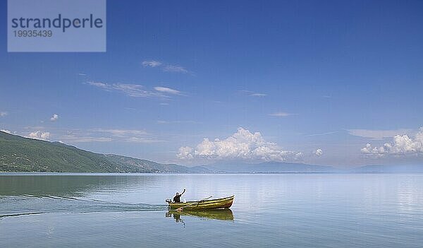 Freundlich winkender Fischer auf einem kleinen Fischerboot  weite Landschaft am Ohridsee  Lin  Albanien  Europa