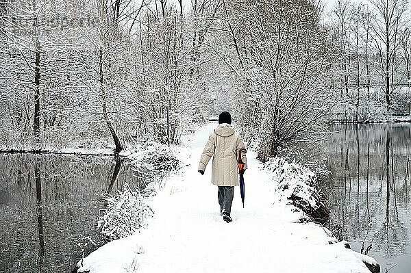 Frau geht auf einem verschneiten Weg zwischen 2 Waldseen