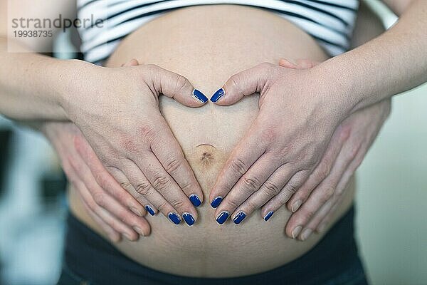 Zwei Paar Hände herzförmig vor dem Babybauch angeordnet