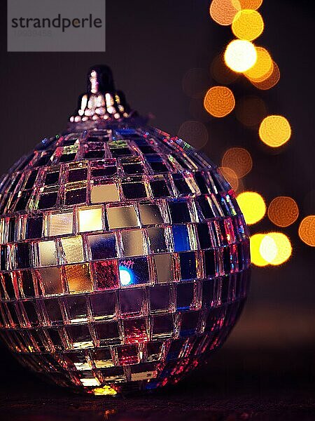 Nahaufnahme einer bunten Disco Weihnachtskugel auf einem Holztisch  verschwommene Weihnachtsbaumbeleuchtung im Hintergrund  schönes Bokeh