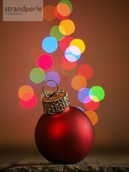 Nahaufnahme einer roten Weihnachtskugel auf einem Holztisch  verschwommene Weihnachtsbaumbeleuchtung im Hintergrund  schönes Bokeh