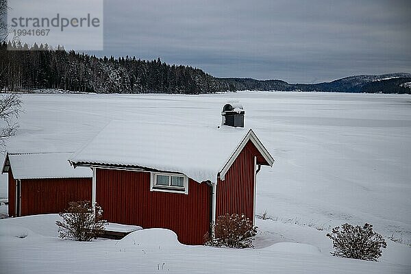 Typisches rotes schwedisches Haus. Holtzhaus in einer Winterlandschaft mit Eis und Schnee. Kleine Siedlung mitten im verschneiten Wald. Landschaftsaufnahme in Schweden