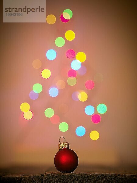Nahaufnahme einer roten Weihnachtskugel auf einem Holztisch  verschwommene Weihnachtsbaumbeleuchtung im Hintergrund  schönes Bokeh