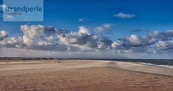 Verlassener Sandstrand mit sanften Wellen  die sich unter einem wolkenverhangenen blaün Himmel an der Küste brechen  idyllisch für einen Sommerurlaub oder einen Kurzurlaub