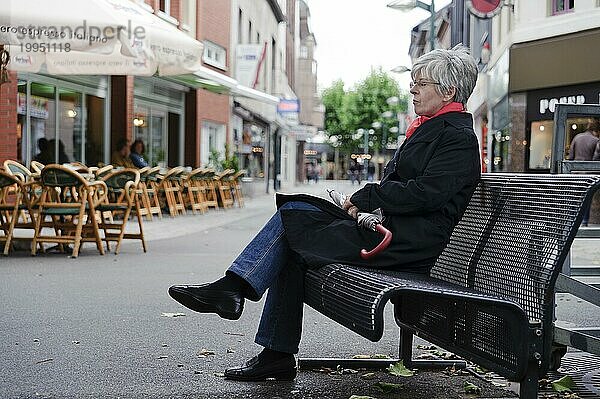 Einsame Frau sitzt mitten in der Stadt allein auf einer Bank